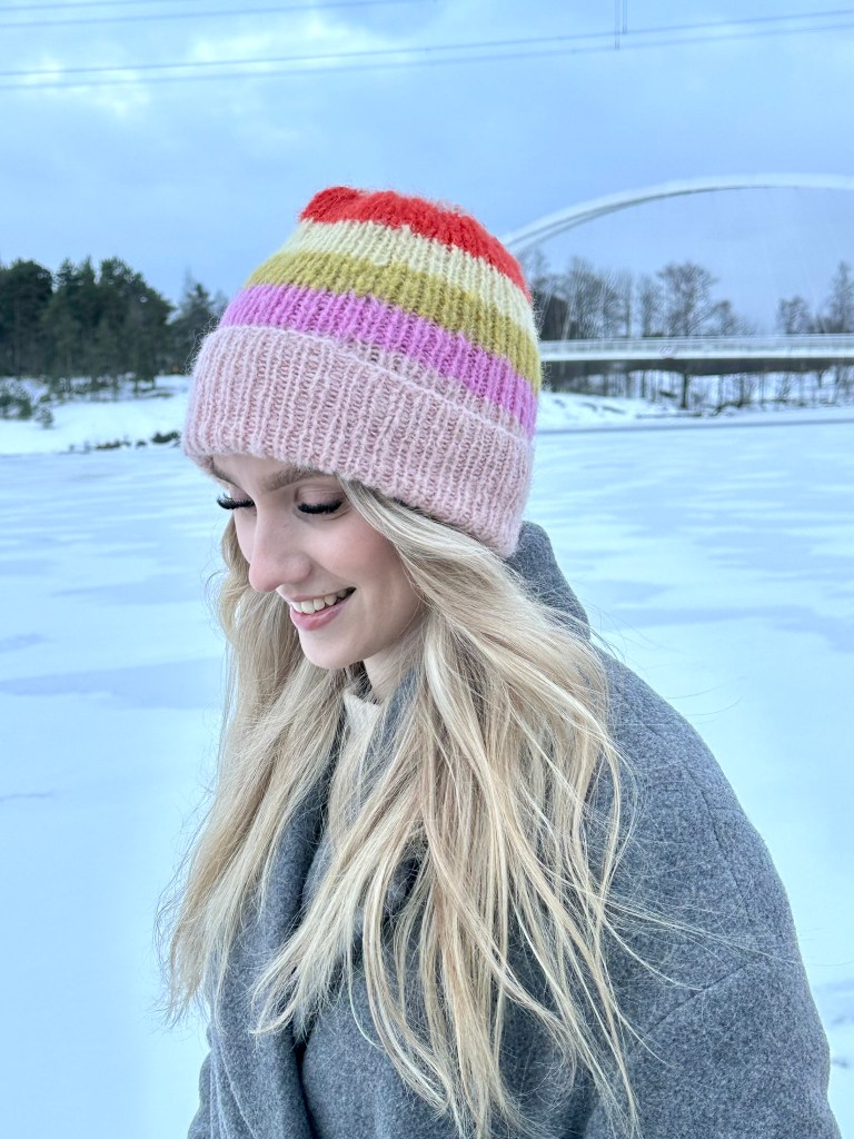 Naisella pinkki, oranssi ja keltaraidallinen Colouriche pipo päässään